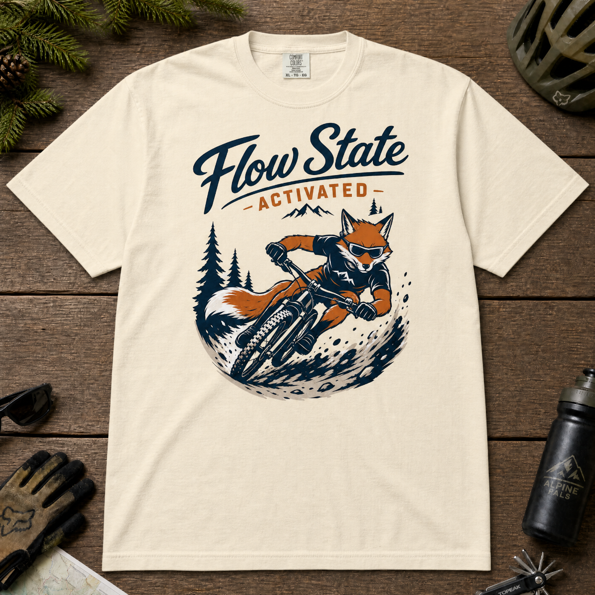 Ivory white t-shirt with a fox riding a bike graphic and 'Flow State Activated' text on a wooden surface.