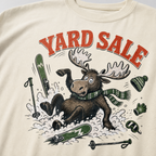 Ivory white t-shirt with moose graphic and 'Yard Sale' text, surrounded by winter accessories on a light background