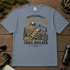 Blue jean colored t-shirt with graphic design of a beaver building a trail, surrounded by outdoor gear on a wooden surface.