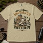 Khaki colored t-shirt with graphic design of a beaver building a trail, surrounded by outdoor gear on a wooden surface.