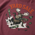 Brick red t-shirt with moose graphic and 'Yard Sale' text, surrounded by winter accessories on a light background
