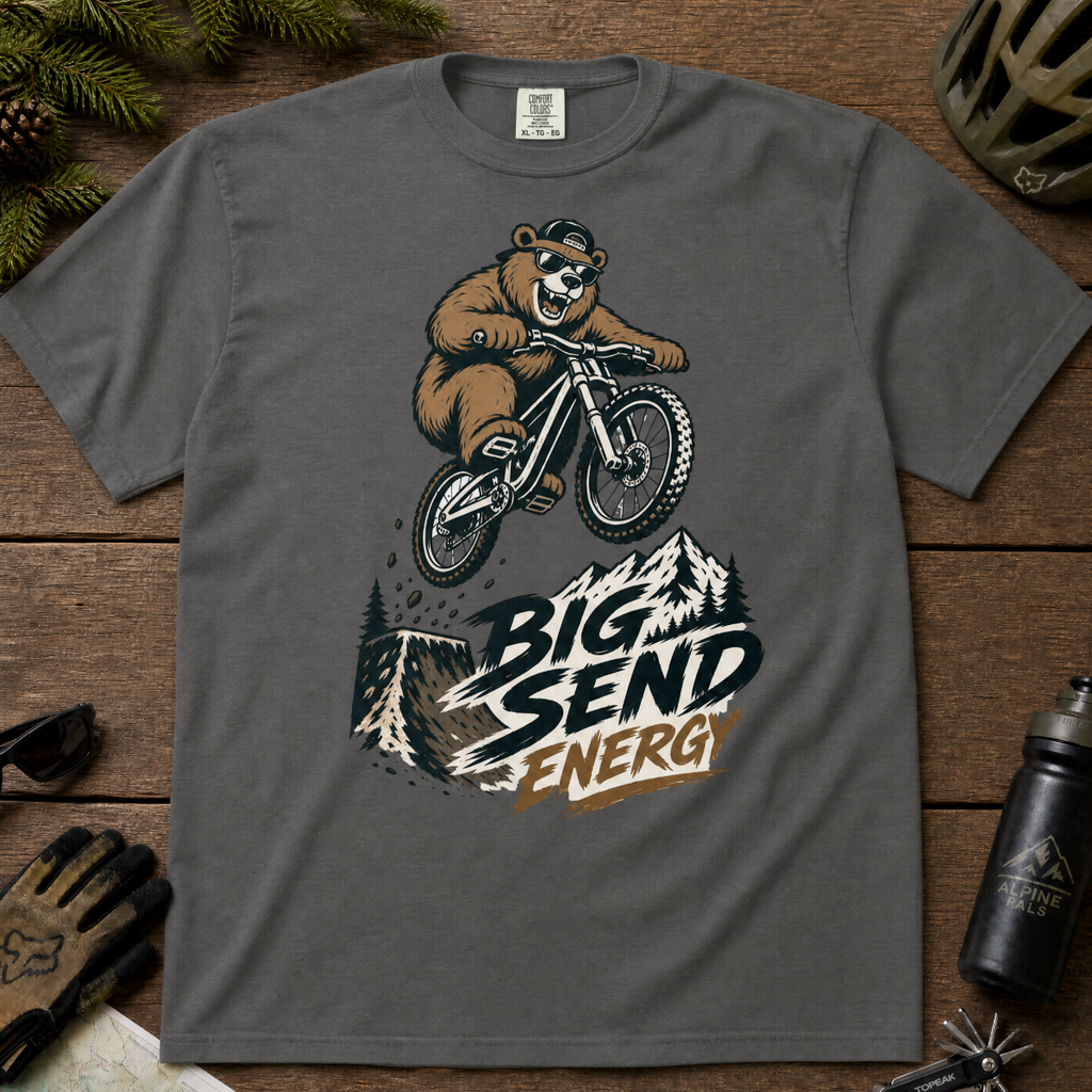 Pepper gray t-shirt with a bear riding a bike graphic and 'Big Send Energy' text on a wooden surface.