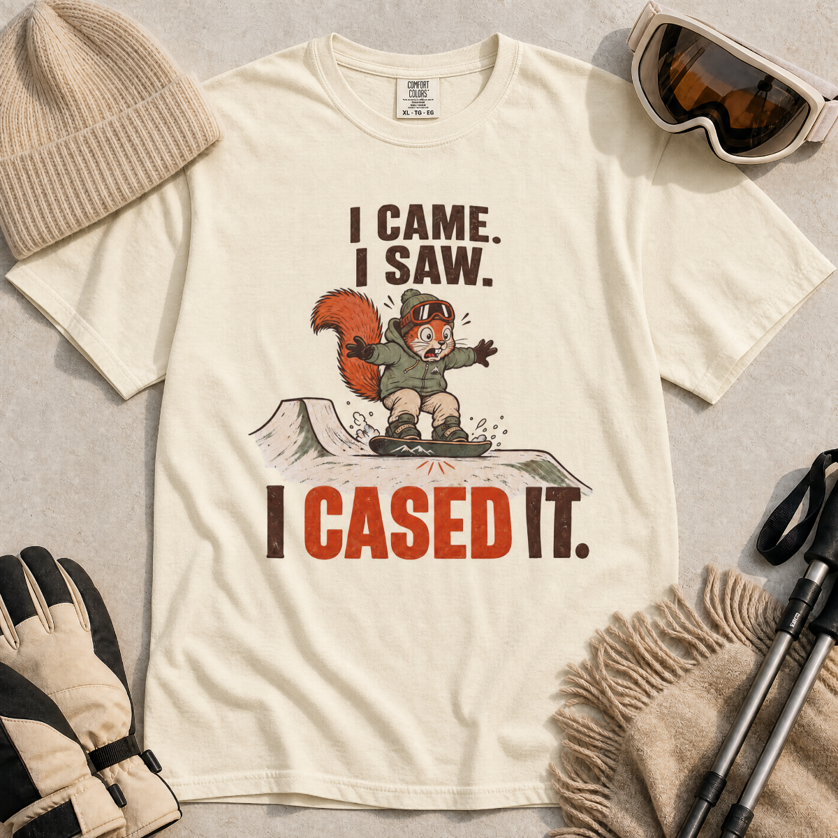Ivory white t-shirt with a graphic of a squirrel and text, surrounded by winter accessories on a light background.