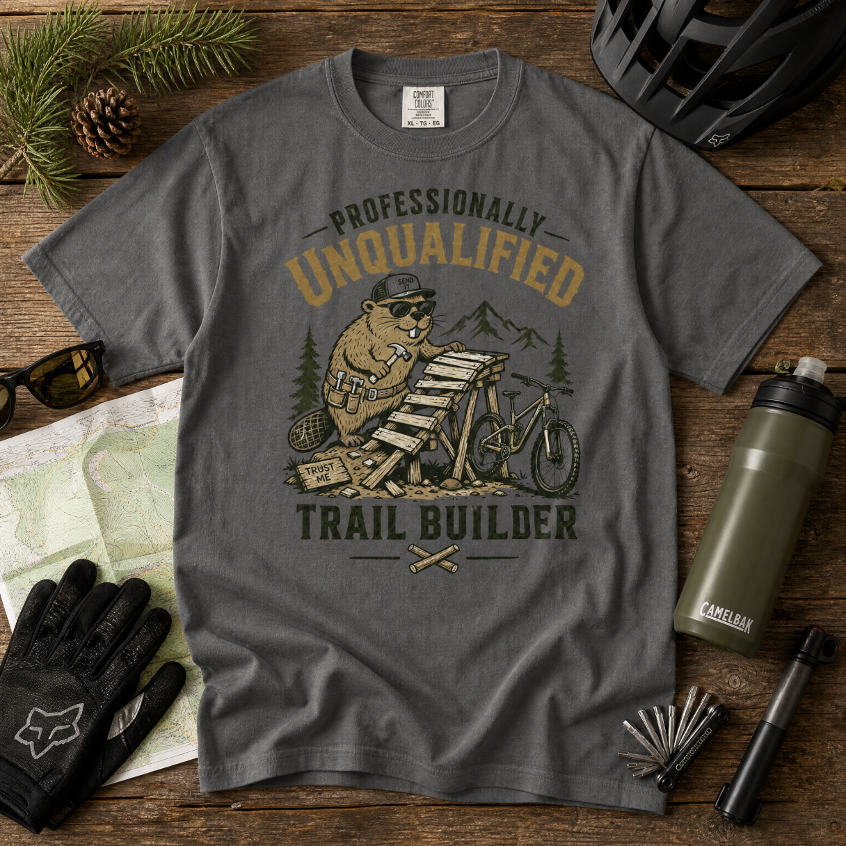 Gray t-shirt with a beaver graphic and text on a wooden surface with outdoor gear.
