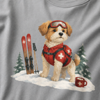 Close-up of a granite gray t-shirt with a sweet ski patrol dog graphic showing a small dog in red rescue gear beside skis and a hot cocoa mug.