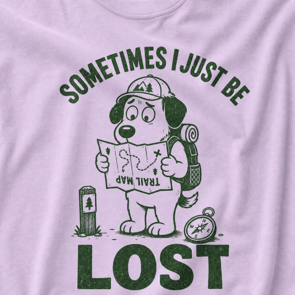 Close-up of an orchid colored t-shirt with a green “Sometimes I Just Be Lost” trail design showing a confused dog reading an upside-down map.