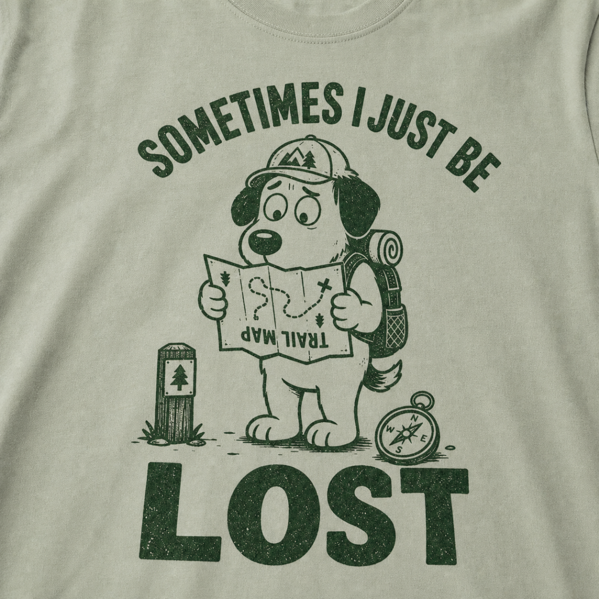 Close-up of a bay green t-shirt with a green “Sometimes I Just Be Lost” trail design showing a confused dog reading an upside-down map.