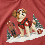 Close-up of a crimson red t-shirt with a sweet ski patrol dog graphic showing a small dog in red rescue gear beside skis and a hot cocoa mug.