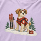 Close-up of an orchid t-shirt with a sweet ski patrol dog graphic showing a small dog in red rescue gear beside skis and a hot cocoa mug.