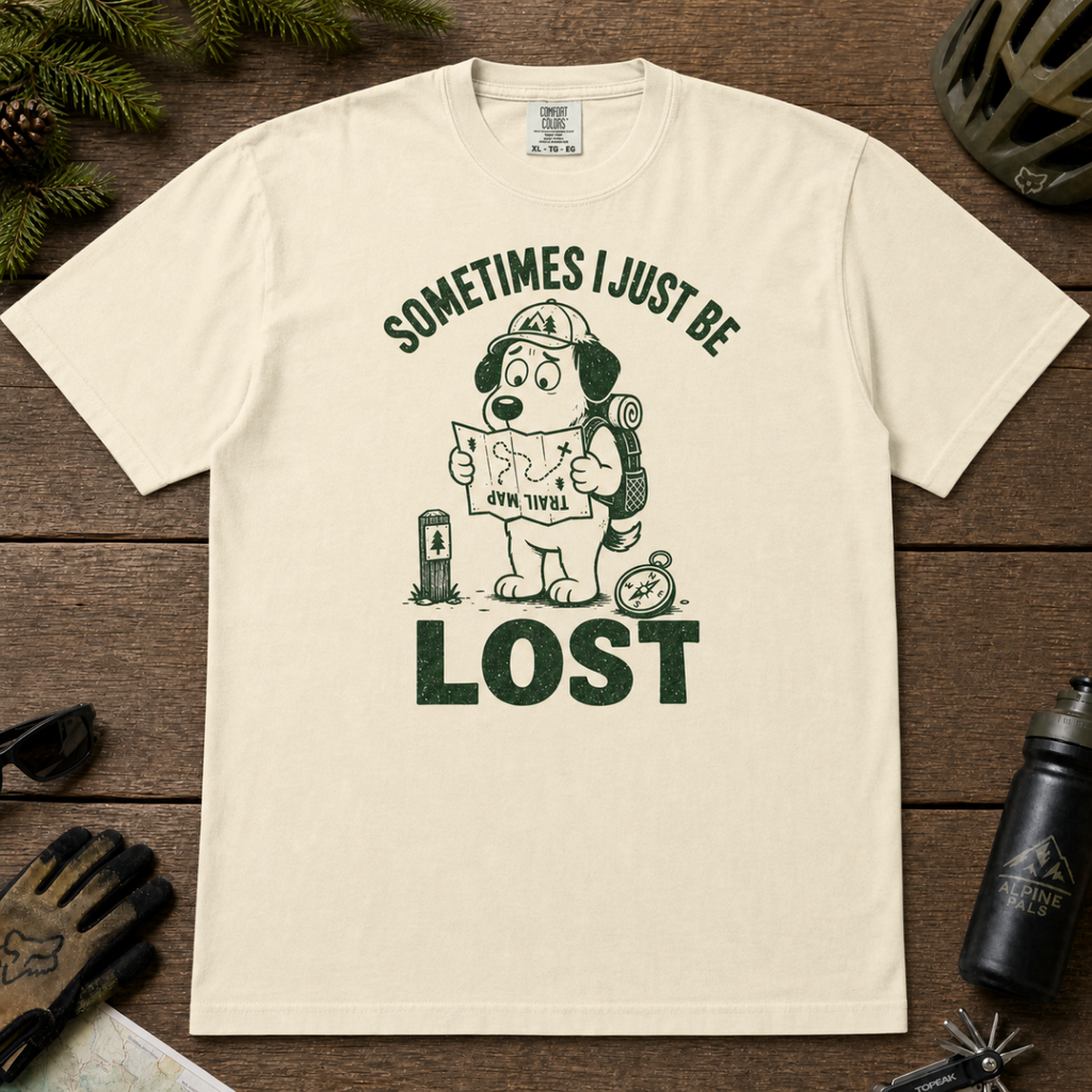 Flat lay of an ivory white t-shirt featuring a funny lost hiker dog graphic with a trail map, compass, backpack, and bold “LOST” text.