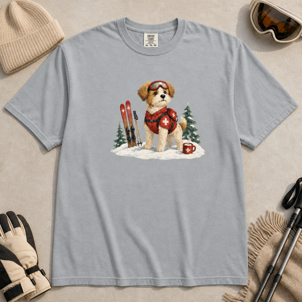 Flat lay of a granite gray t-shirt featuring a cute ski patrol dog design with red rescue gear, skis, snowy trees, and a hot cocoa mug.