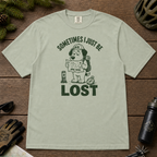 Flat lay of a bay green t-shirt featuring a funny lost hiker dog graphic with a trail map, compass, backpack, and bold “SOMETIMES I JUST BE LOST” text.