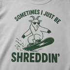 Close-up of a granite gray t-shirt with a simple green snowboard goat graphic and bold “Sometimes I Just Be Shreddin’” text.