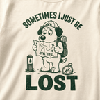Close-up of an ivory white t-shirt with a green “Sometimes I Just Be Lost” trail design showing a confused dog reading an upside-down map.
