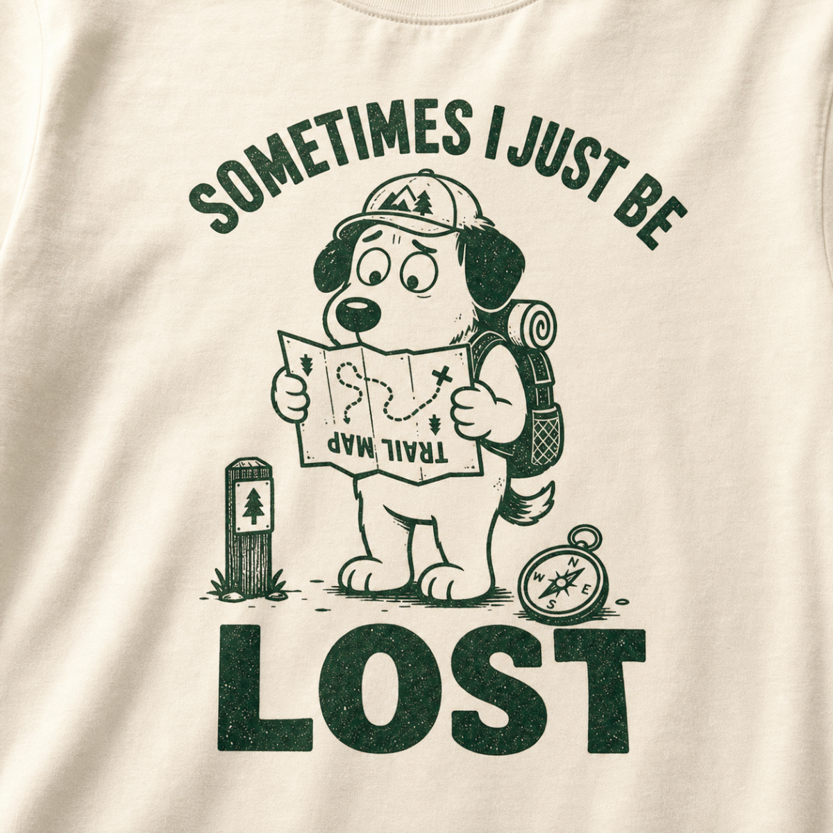 Close-up of an ivory white t-shirt with a green “Sometimes I Just Be Lost” trail design showing a confused dog reading an upside-down map.
