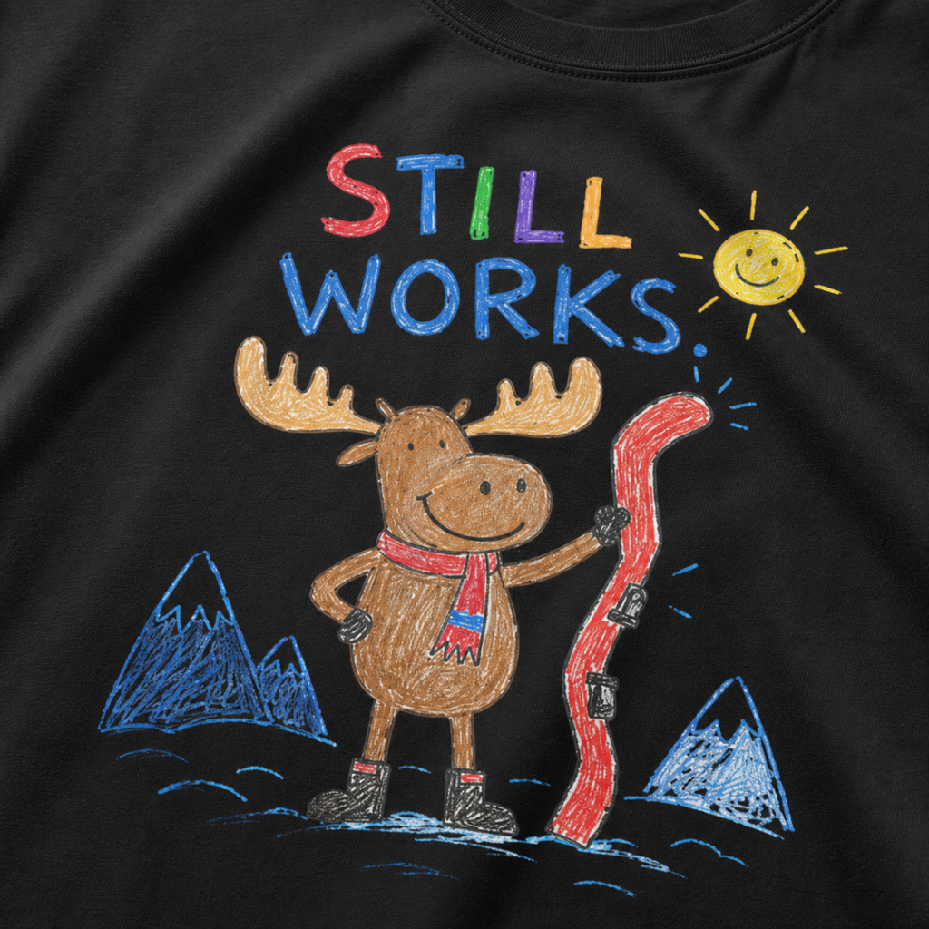 Close-up of a black t-shirt with a playful crayon-style ski design showing a smiling moose holding a red ski, with “Still Works.” text.