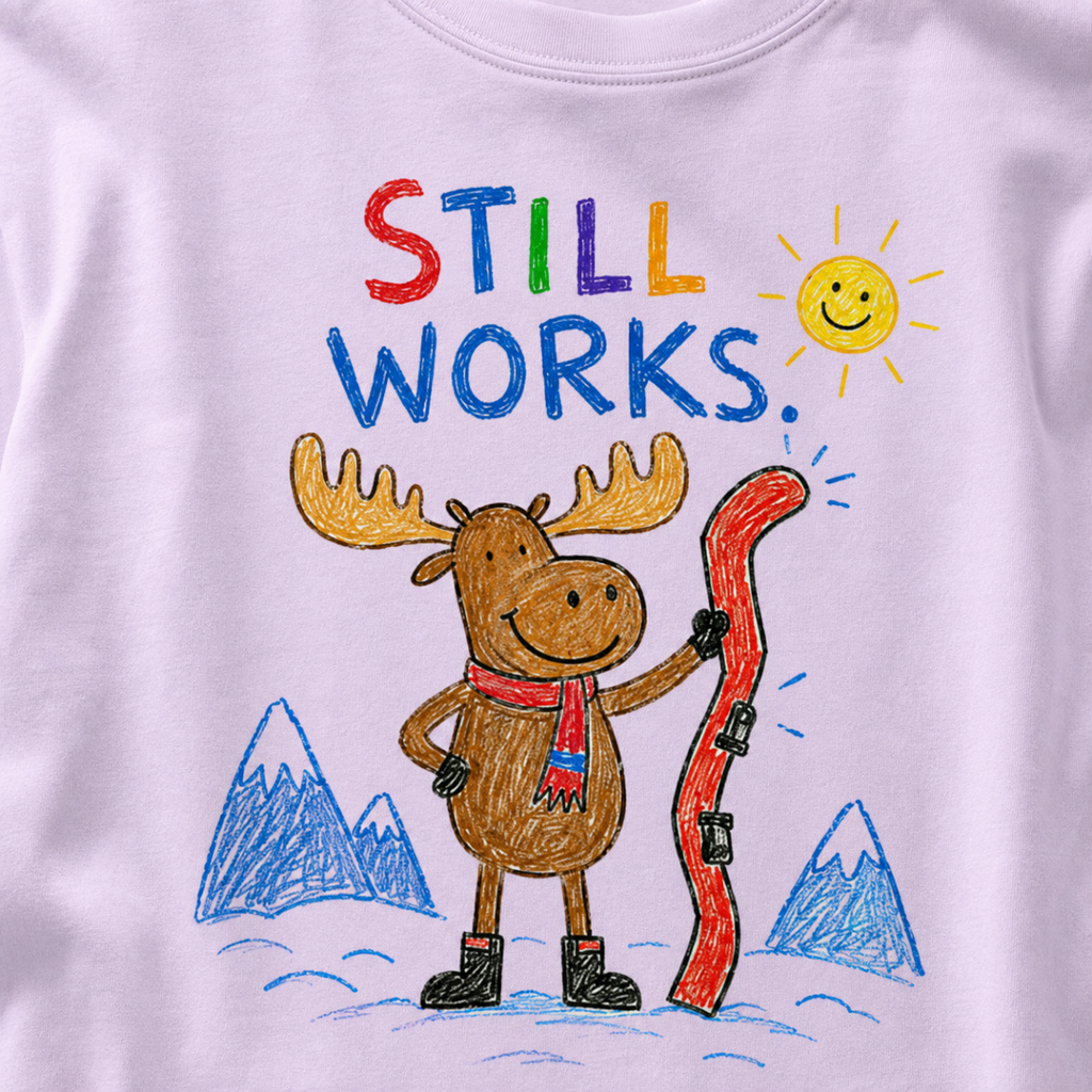 Close-up of an orchid t-shirt with a playful crayon-style ski design showing a smiling moose holding a red ski, with “Still Works.” text.