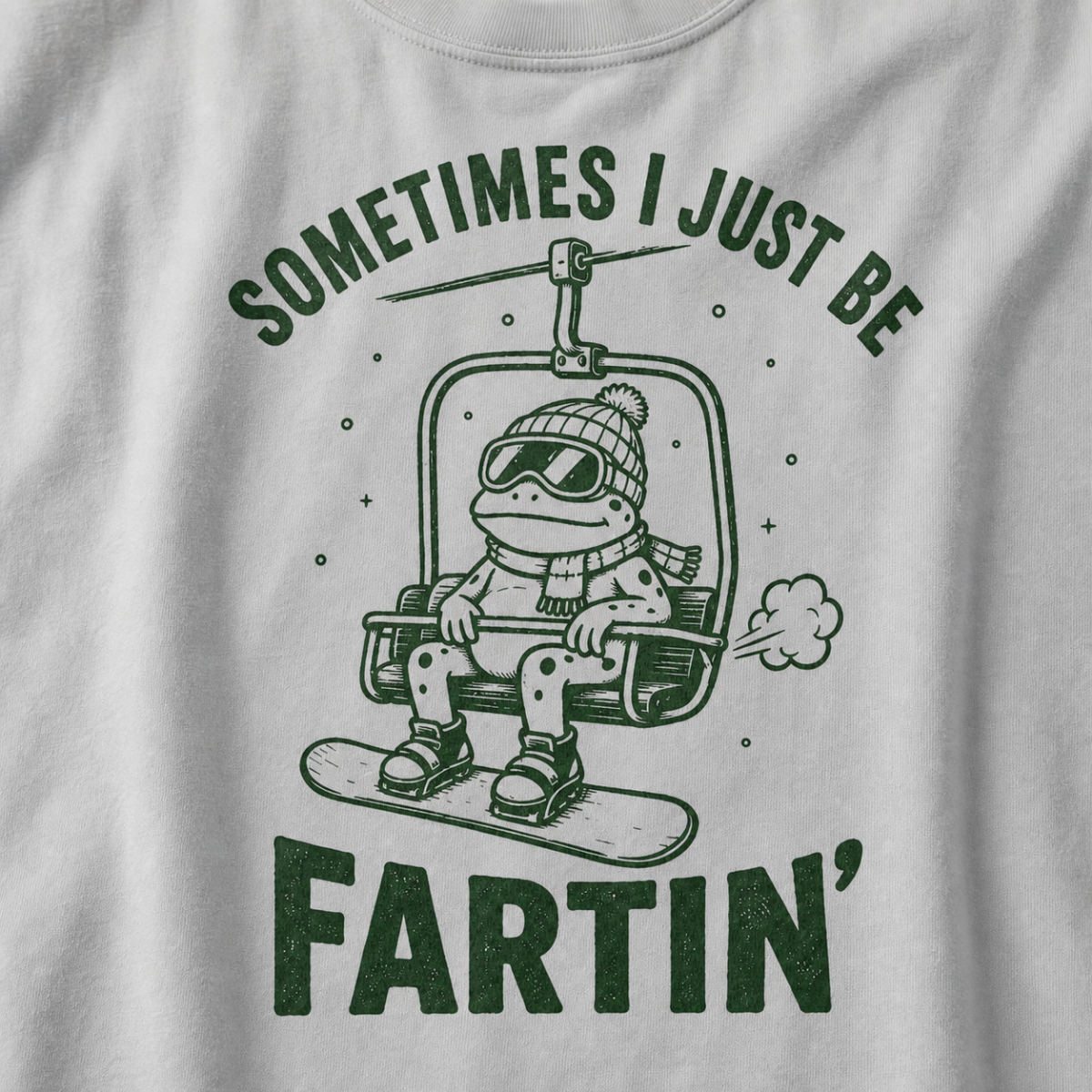 Close-up of a granite gray t-shirt with a playful frog chairlift graphic and bold “Sometimes I Just Be Fartin’” text.