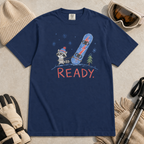 Flat lay of a navy t-shirt featuring a childlike crayon-style design with a small raccoon pulling a blue snowboard and bold “READY.” text.