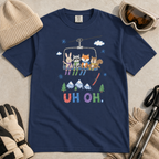 Flat lay of a navy t-shirt featuring a playful hand-drawn chairlift scene with bunny, raccoon, fox, and squirrel skiers, snowy mountains, and “UH OH.” text.