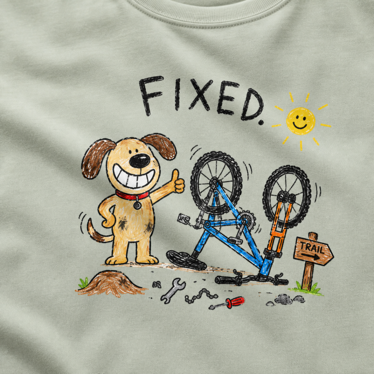 Close-up of a bay green t-shirt with a playful hand-drawn dog giving a thumbs up beside a repaired upside-down bike, scattered tools, and “FIXED.” text.
