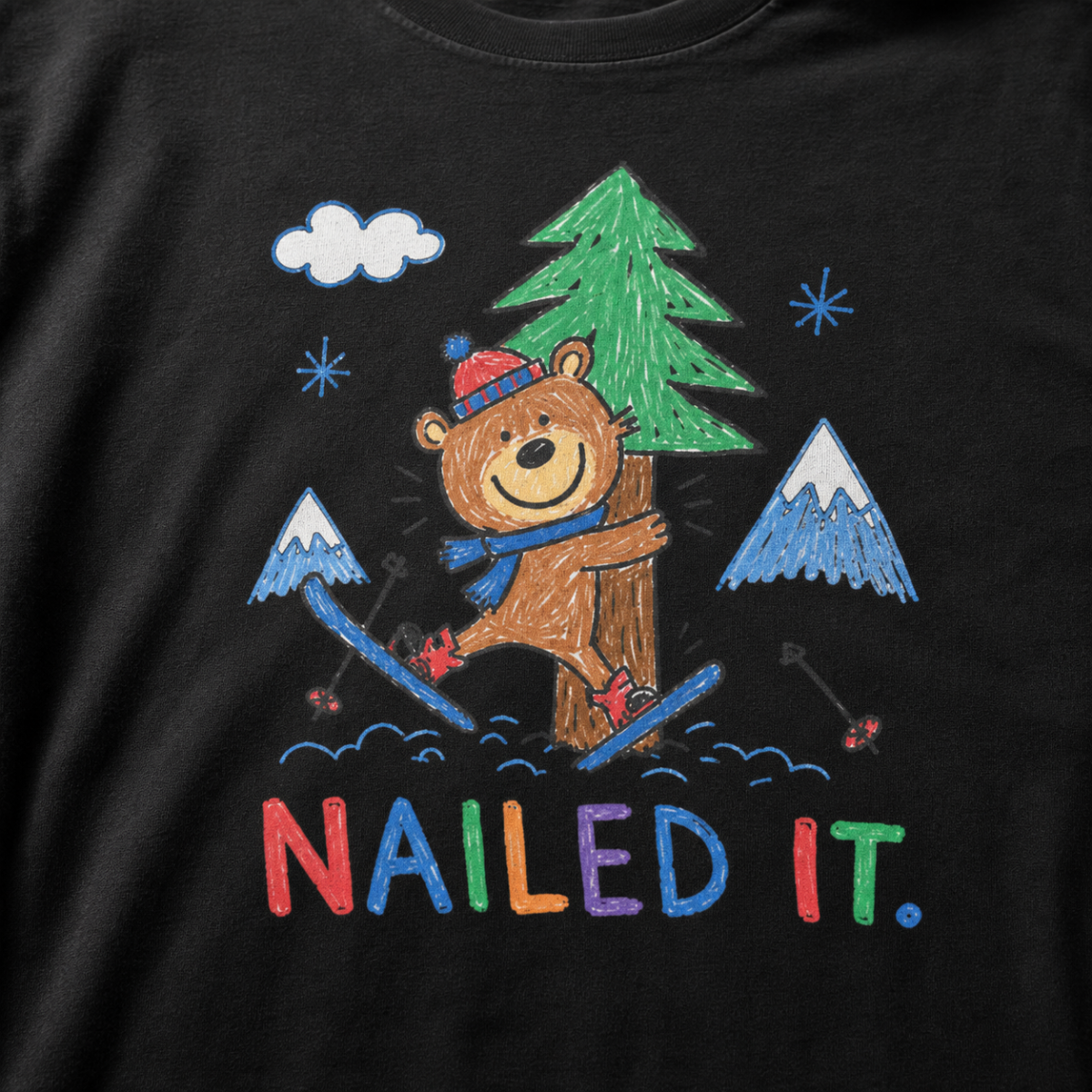 Close-up of a black t-shirt with a childlike crayon-style ski design showing a smiling bear hugging a tree, with colorful “Nailed It.” text.