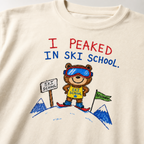 Close-up of an ivory white t-shirt with a playful hand-drawn bear at ski school, beginner flag, mountain details, and “I Peaked in Ski School.” text.