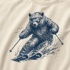 Close-up of an ivory white t-shirt with a dynamic bear skier graphic showing the bear carving through snow with goggles and ski poles.