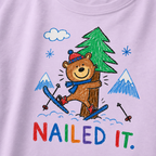 Close-up of an orchid t-shirt with a childlike crayon-style ski design showing a smiling bear hugging a tree, with colorful “Nailed It.” text.