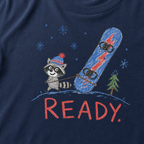 Close-up of a navy t-shirt with a playful hand-drawn raccoon snowboarding graphic, snowflakes, a pine tree, and large red “READY.” text.