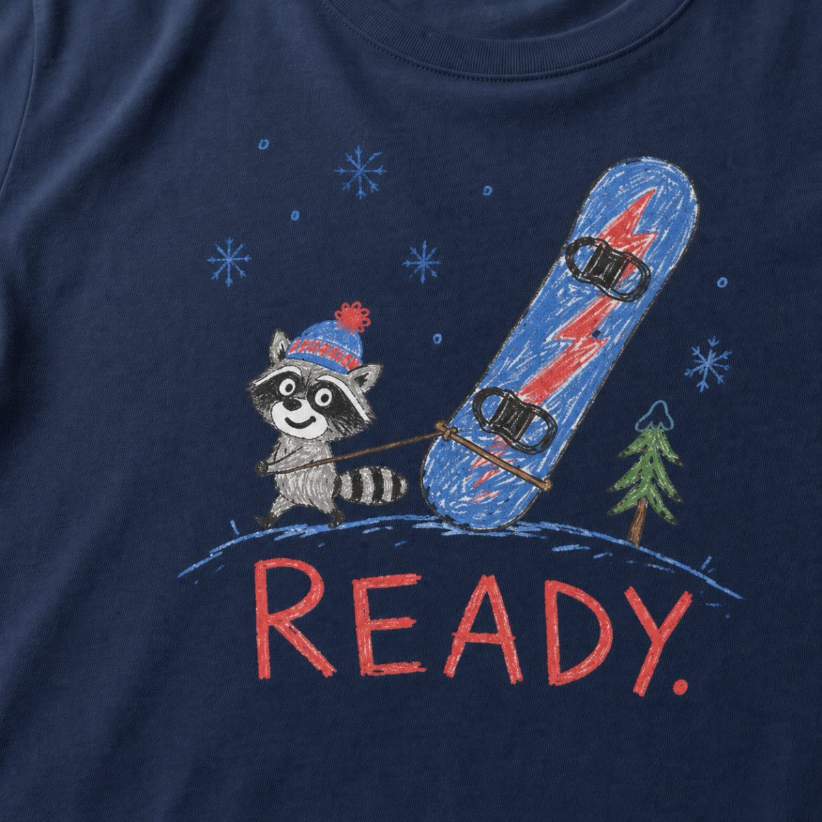 Close-up of a navy t-shirt with a playful hand-drawn raccoon snowboarding graphic, snowflakes, a pine tree, and large red “READY.” text.