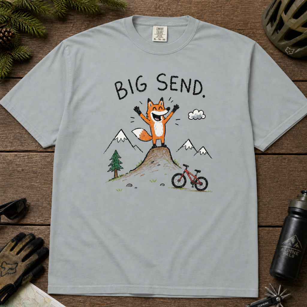 Flat lay of a granite gray t-shirt featuring a playful hand-drawn fox mountain bike graphic with mountains, a small bike, and “Big Send.” text.