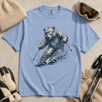 Flat lay of a washed denim blue t-shirt featuring a detailed blue line-art bear skiing through powder, styled with winter accessories.