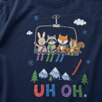 Close-up of a navy t-shirt with a childlike crayon-style ski design showing four animals on a chairlift, a loose red ski falling below, and colorful “UH OH.” text.