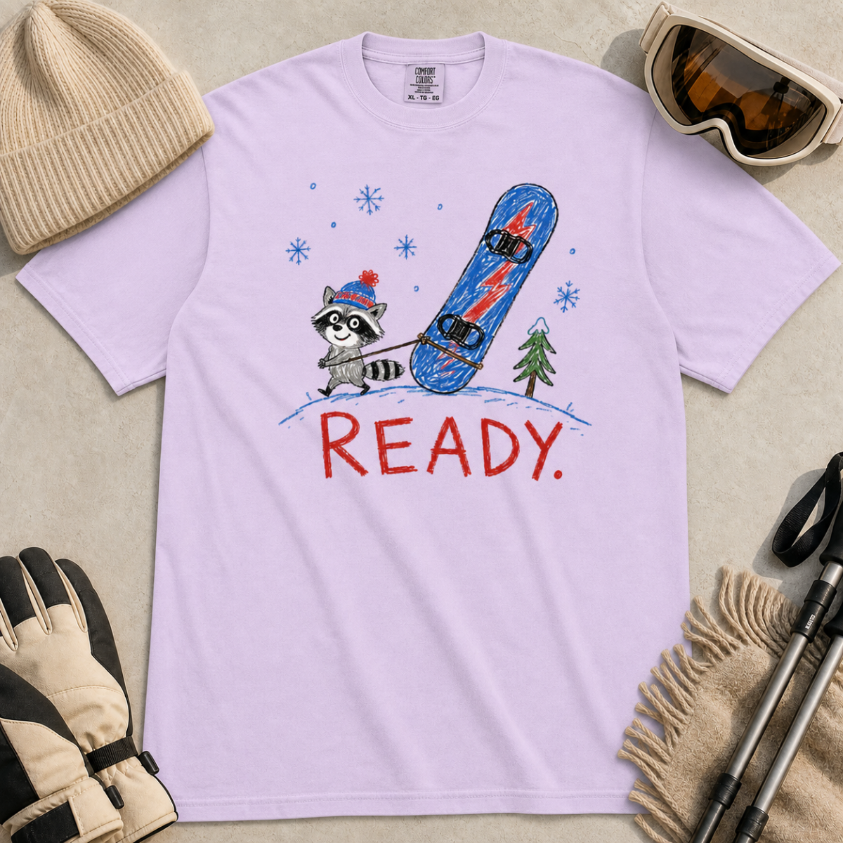 Flat lay of an orchid t-shirt featuring a childlike crayon-style design with a small raccoon pulling a blue snowboard and bold “READY.” text.