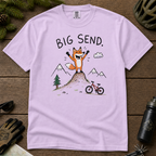 Flat lay of an orchid t-shirt featuring a playful hand-drawn fox mountain bike graphic with mountains, a small bike, and “Big Send.” text.