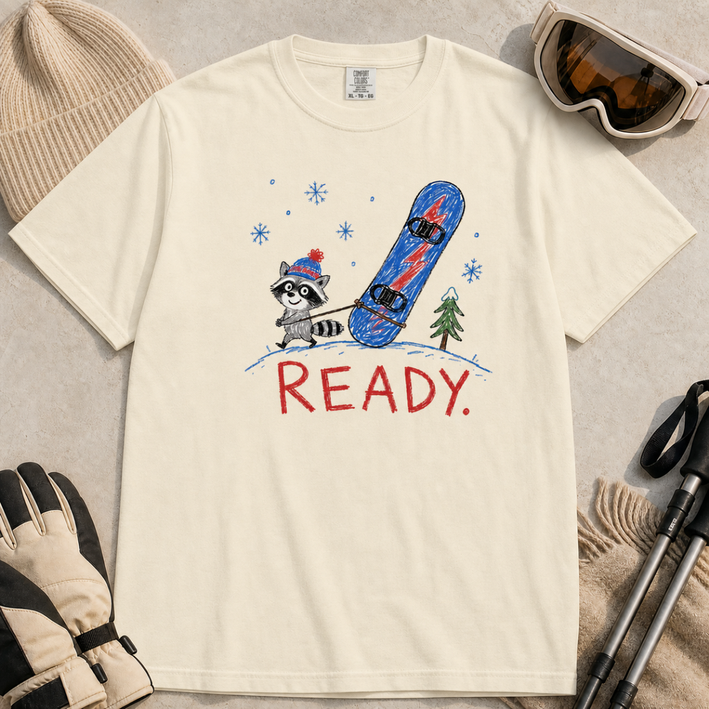 Flat lay of an ivory white t-shirt featuring a childlike crayon-style design with a small raccoon pulling a blue snowboard and bold “READY.” text.