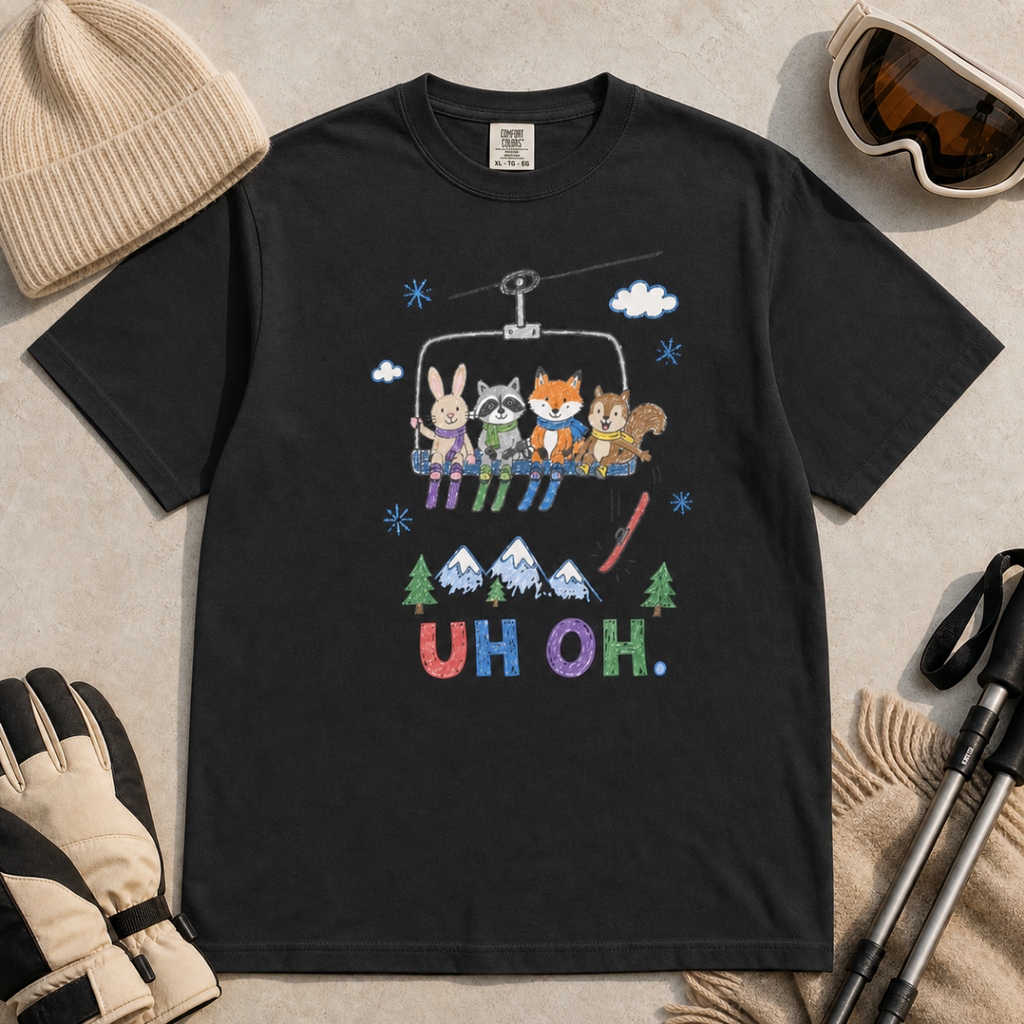 Flat lay of a black t-shirt featuring a playful hand-drawn chairlift scene with bunny, raccoon, fox, and squirrel skiers, snowy mountains, and “UH OH.” text.