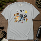 Flat lay of a granite gray t-shirt featuring a childlike crayon-style bike repair design with a smiling dog, upside-down mountain bike, tools, and “FIXED.” text.