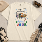 Flat lay of an ivory white t-shirt featuring a playful hand-drawn chairlift scene with bunny, raccoon, fox, and squirrel skiers, snowy mountains, and “UH OH.” text.