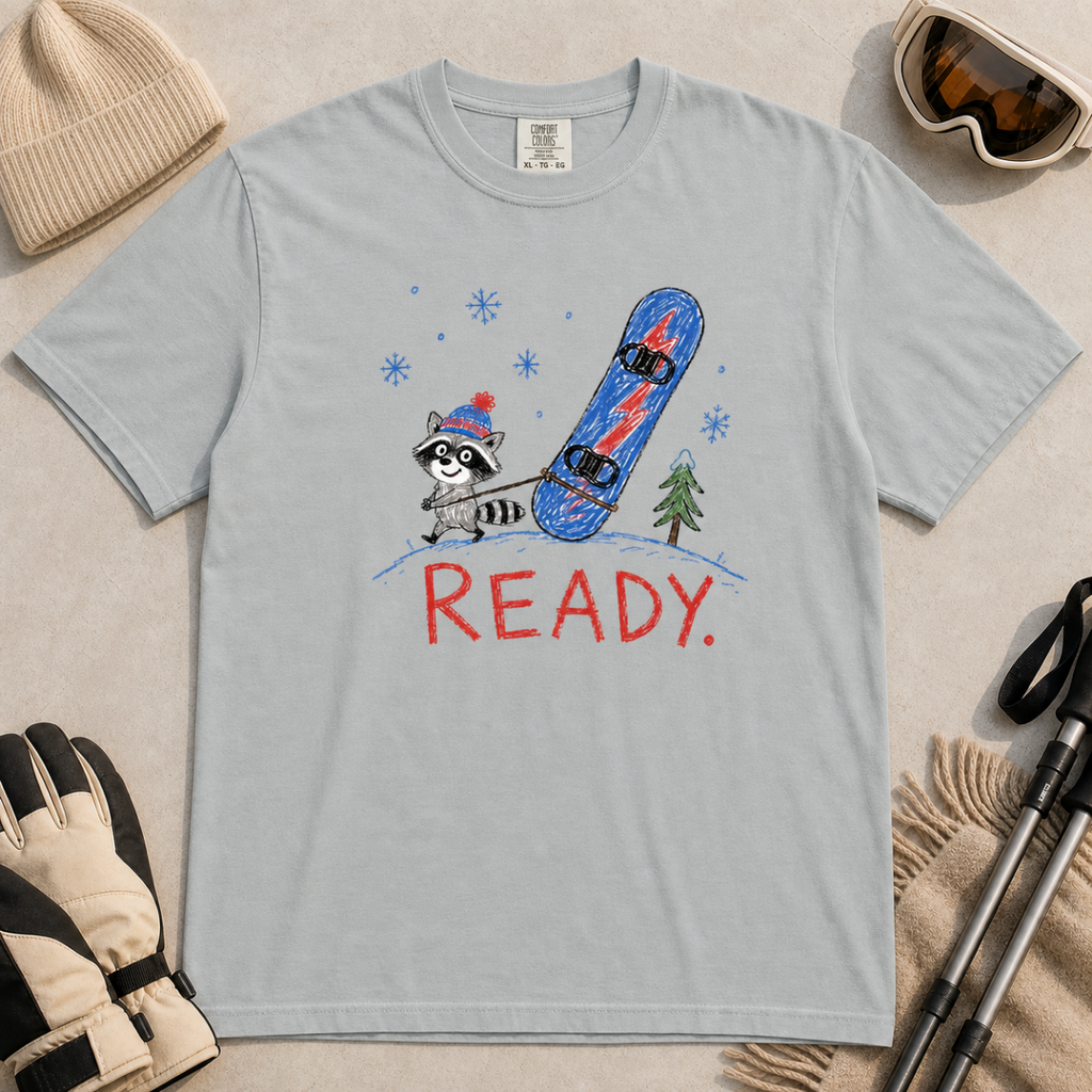 Flat lay of a granite gray t-shirt featuring a childlike crayon-style design with a small raccoon pulling a blue snowboard and bold “READY.” text.