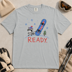 Flat lay of a granite gray t-shirt featuring a childlike crayon-style design with a small raccoon pulling a blue snowboard and bold “READY.” text.