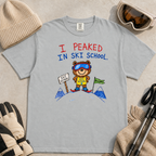 Flat lay of a granite gray t-shirt featuring a childlike crayon-style ski design with a proud bear in ski school gear and “I Peaked in Ski School.” text.