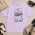 Flat lay of an orchid t-shirt featuring a playful hand-drawn chairlift scene with bunny, raccoon, fox, and squirrel skiers, snowy mountains, and “UH OH.” text.