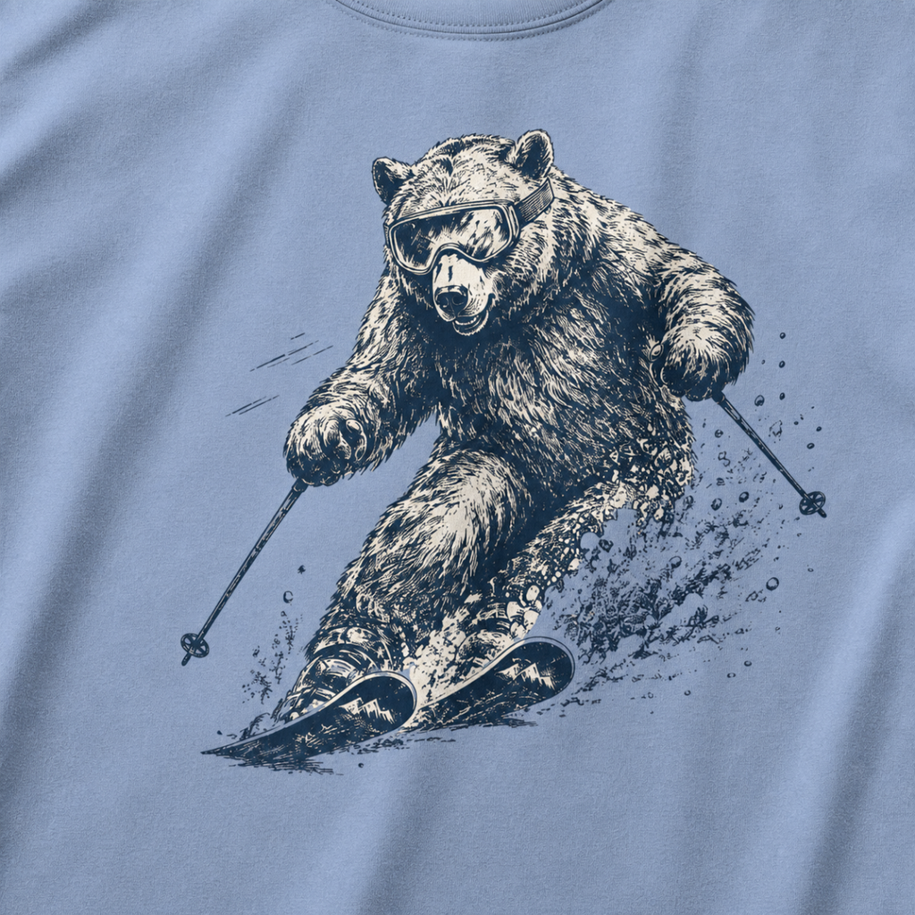 Close-up of a washed denim blue t-shirt with a dynamic bear skier graphic showing the bear carving through snow with goggles and ski poles.