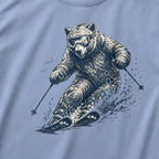 Close-up of a washed denim blue t-shirt with a dynamic bear skier graphic showing the bear carving through snow with goggles and ski poles.