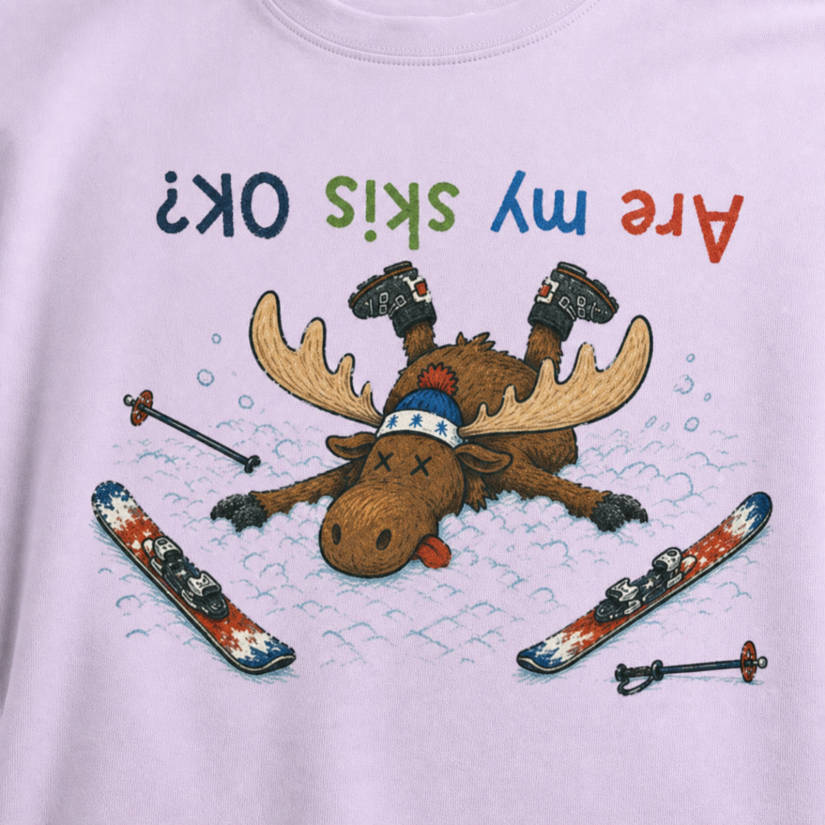 Close-up of an orchid t-shirt showing a crashed moose lying upside down in the snow with loose ski gear and colorful “Are My Skis OK?” text.
