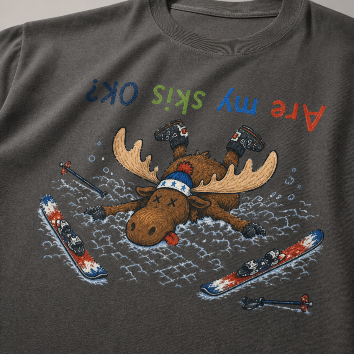 Close-up of a pepper gray t-shirt showing a crashed moose lying upside down in the snow with loose ski gear and colorful “Are My Skis OK?” text.