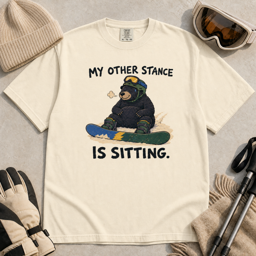 Flat lay of an ivory white t-shirt with a humorous snowboarding design showing a resting bear seated behind its board.