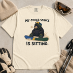 Flat lay of an ivory white t-shirt with a humorous snowboarding design showing a resting bear seated behind its board.